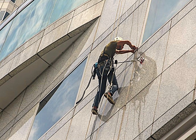 Técnico en trabajos verticales realizando limpieza y saneamiento de fachada de piedra sin andamios.