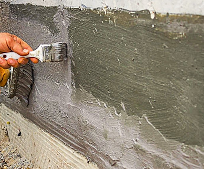 Aplicación manual de mortero técnico impermeabilizante en zócalo de fachada para protección contra la humedad por capilaridad.