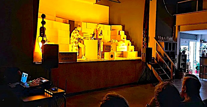 Técnico de sonido con sello de Innovagroup y equipo de iluminación en un montaje teatral íntimo con actores sobre cajas.