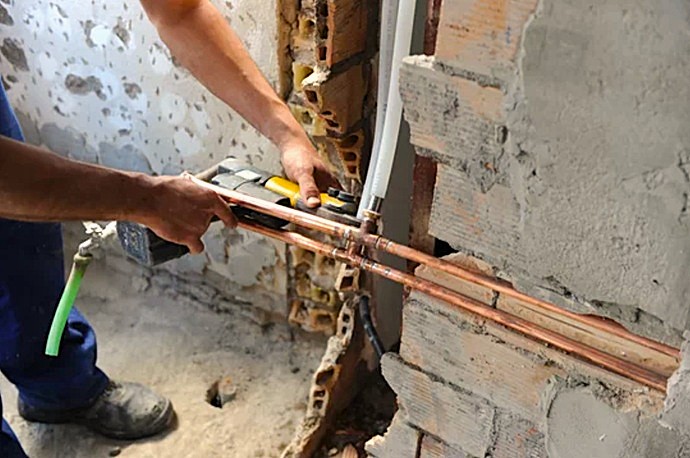 Técnico realizando prensado mecánico de alta precisión en codo de tubería de cobre.