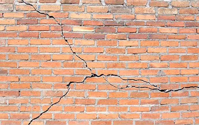 Grieta profunda diagonal en muro de ladrillo caravista por fatiga estructural.