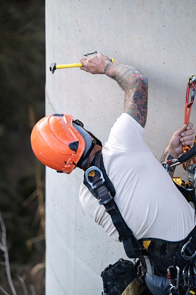 Albañil en suspensión ejecutando consolidación de pilar de hormigón mediante técnica de picado y saneamiento.