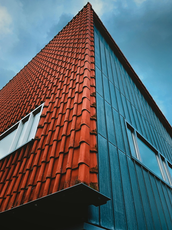 El vértice de la casa con tejas rojas y panelado metálico oscuro, contrastando entre la tradición del barro y la modernidad de los cerramientos industriales.