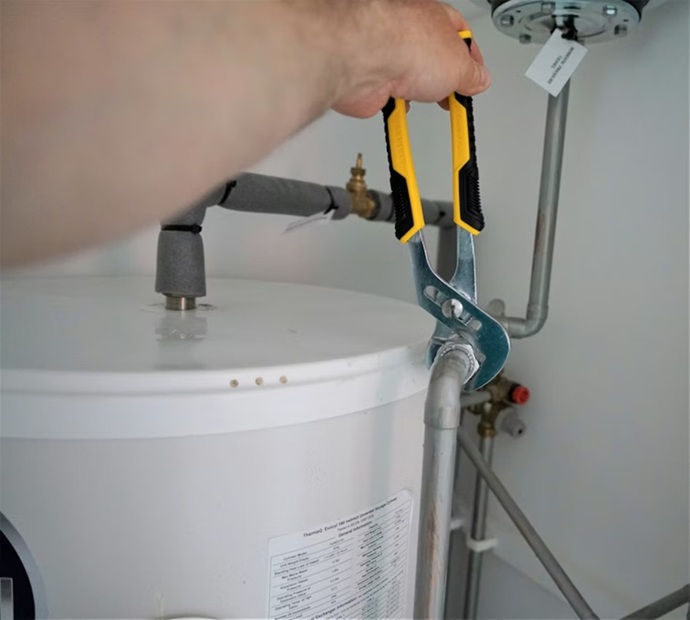 Técnico especialista realizando una inspección ocular con iluminación focalizada en la base de un termo eléctrico para detectar calcificación.