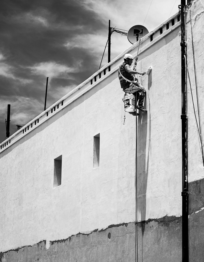 Operario en suspensión aplicando pintura técnica protectora en paramento de gran altura sin estructuras metálicas.