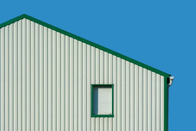 Cerramiento superior y lateral de nave industrial con panel sándwich nervado color crema y perfiles verdes.