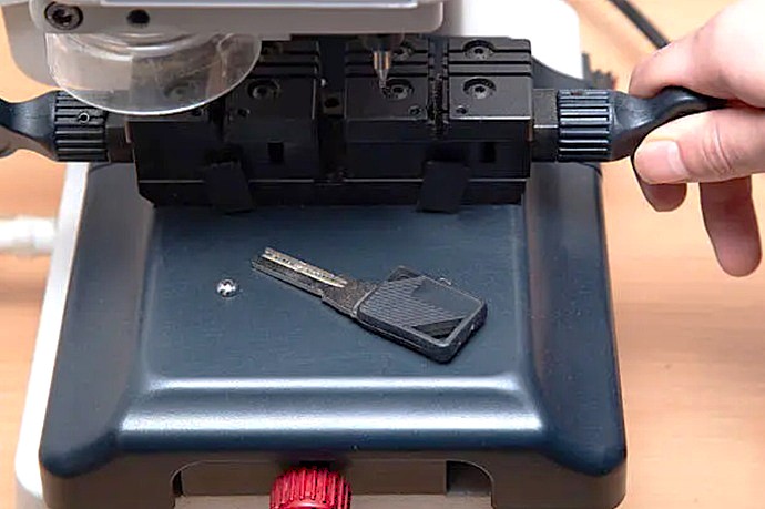 Tallado de precisión de llave vehicular mediante fresadora electrónica de alta fidelidad en laboratorio técnico.