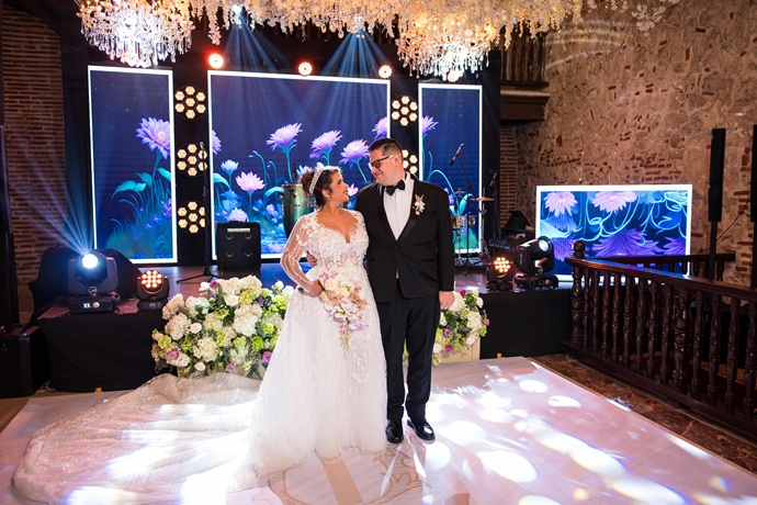 Pareja nupcial frente a un panel visual de alta gama flanqueados por lámparas de cristal e iluminación arquitectónica en tonos índigo.