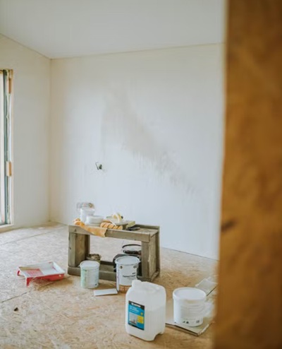 Estancia en fase de preparación para pintura técnica con cubos de materiales y mobiliario protegido.