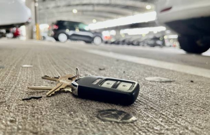 Llavero de coche moderno extraviado sobre el firme de un estacionamiento, reflejando una pérdida de acceso inminente.