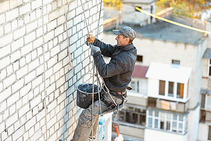 Técnico cualificado reparando albañilería vertical sobre ladrillo mediante posicionamiento por cuerdas.