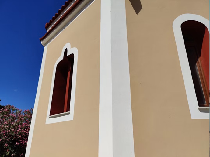 Paramento exterior restaurado en tono ocre con recercados blancos impolutos que resaltan arcos arquitectónicos tradicionales bajo un cielo mediterráneo.