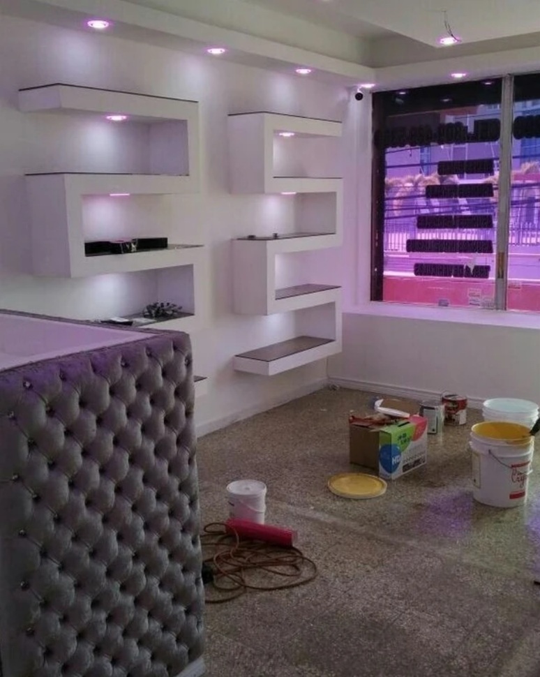 Mueble de mostrador en capitoné gris acero y estanterías en serpentina iluminadas con LED bajo foseados de techo.