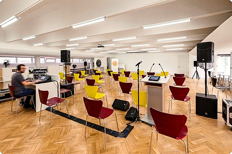 Técnico operando mesa de sonido digital en sala de conferencias para formación corporativa de tamaño medio.