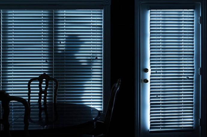Silueta de un intruso acechando en el exterior de una vivienda a través de una persiana veneciana