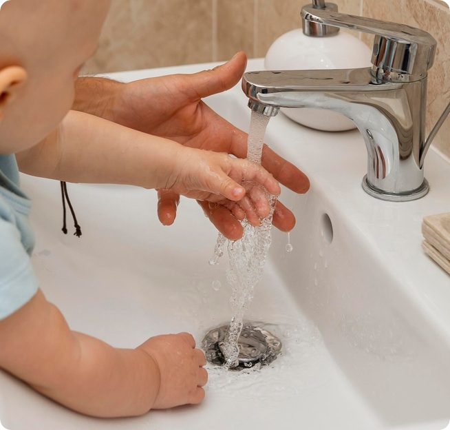 Manos adultas y dee bebé lavándose con agua corriente de caudal limpio.