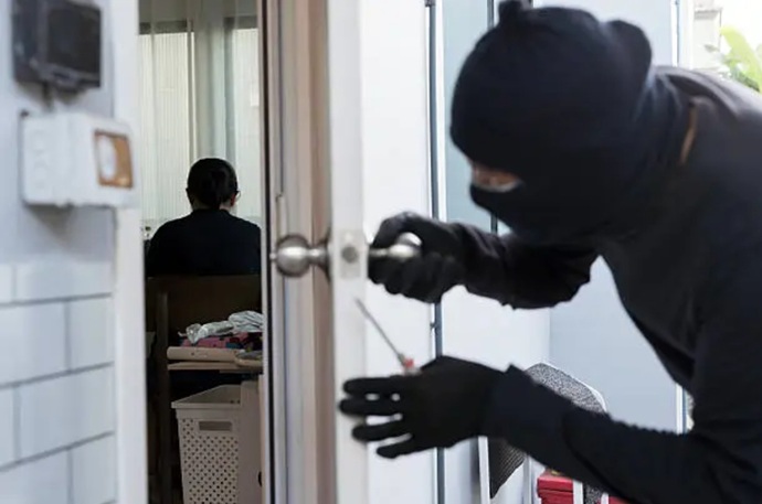 Intruso encapuchado manipulando la cerradura de una puerta mediante ganzuado en un piso de Gràcia.